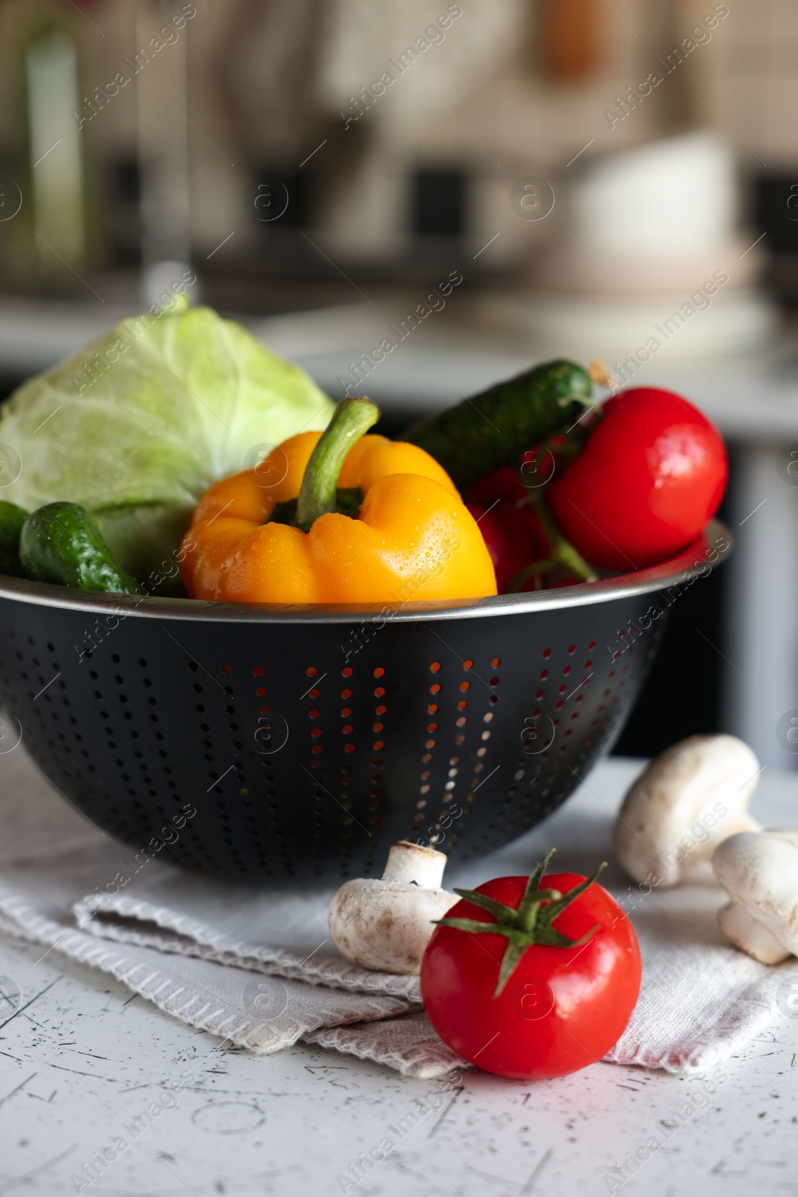 Photo of Metal colander with different wet vegetables on white textured table, closeup