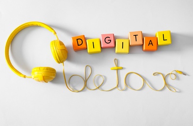 Photo of Words DIGITAL DETOX made with colorful cubes and wire of headphones on white background, top view