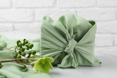 Photo of Furoshiki technique. Gift packed in green fabric and plants for decor on white table
