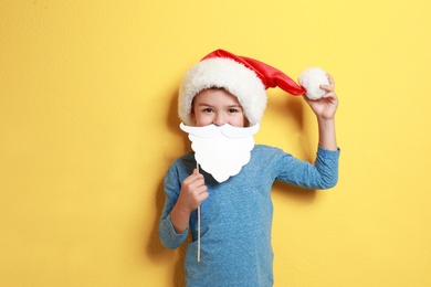 Image of Cute little boy with Santa hat and white beard prop on yellow background. Christmas celebration