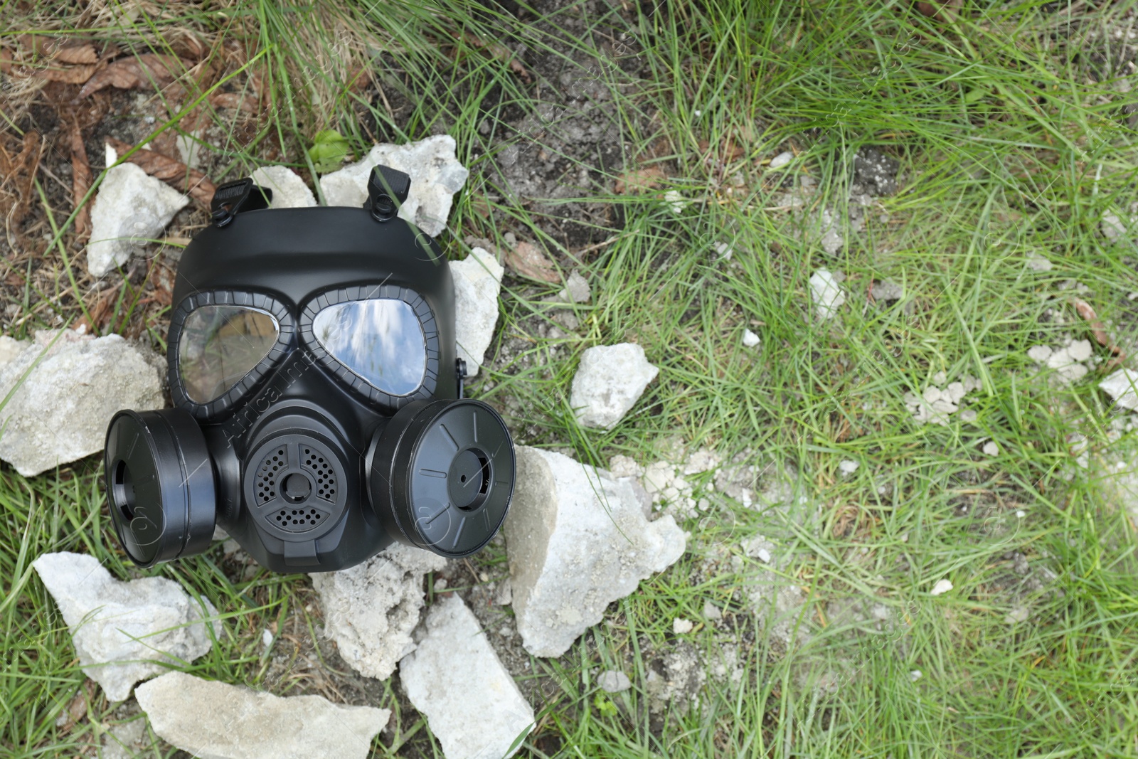 Photo of One gas mask on ground with stones outdoors, top view. Space for text