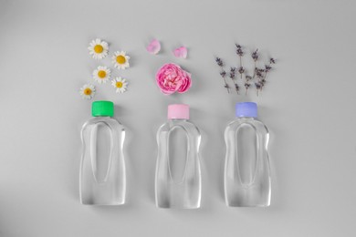 Bottles with baby oil and flowers on light grey background, flat lay. Space for text