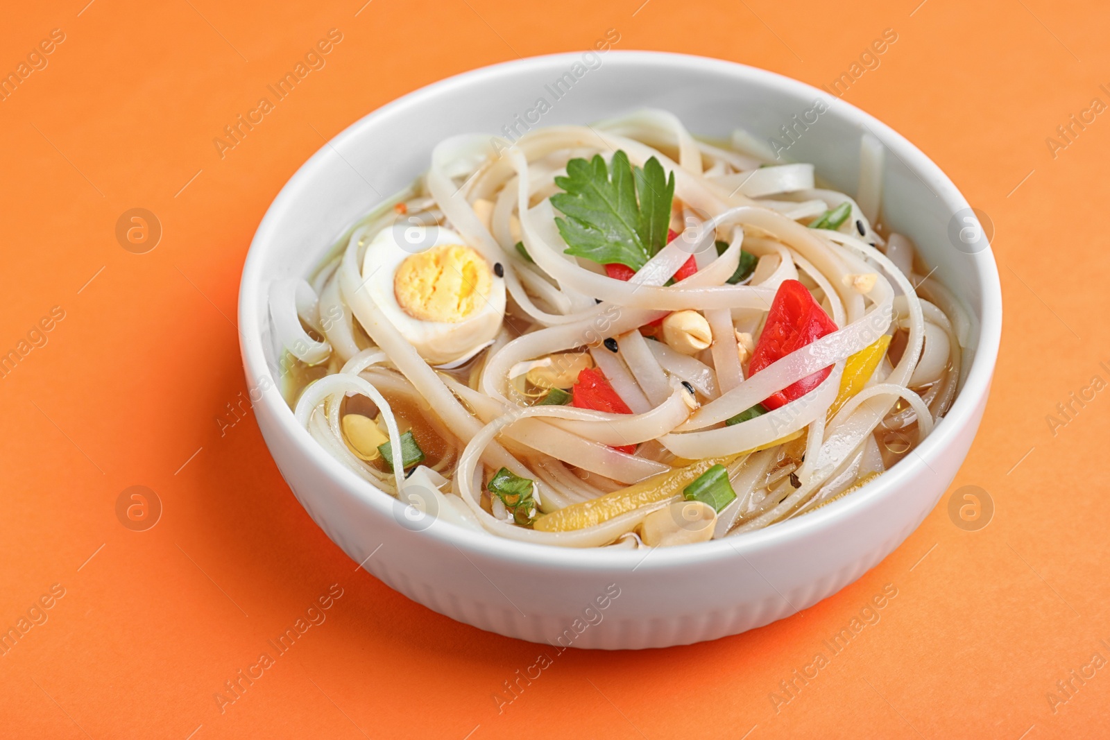 Photo of Tasty ramen with rice noodles and vegetables on orange background