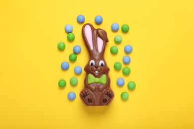 Chocolate Easter bunny and candies on yellow background, flat lay