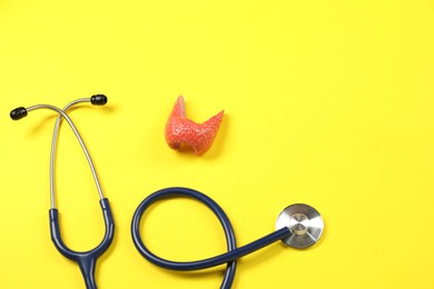 Photo of Endocrinology. Stethoscope and model of thyroid gland on yellow background, above view. Space for text