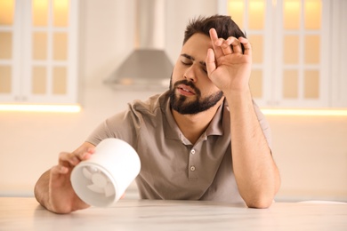 Photo of Man with portable fan suffering from heat at home. Summer season