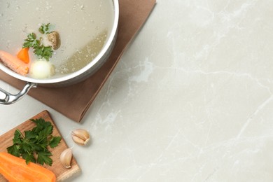 Pot with delicious bone broth and ingredients on light grey table, flat lay. Space for text