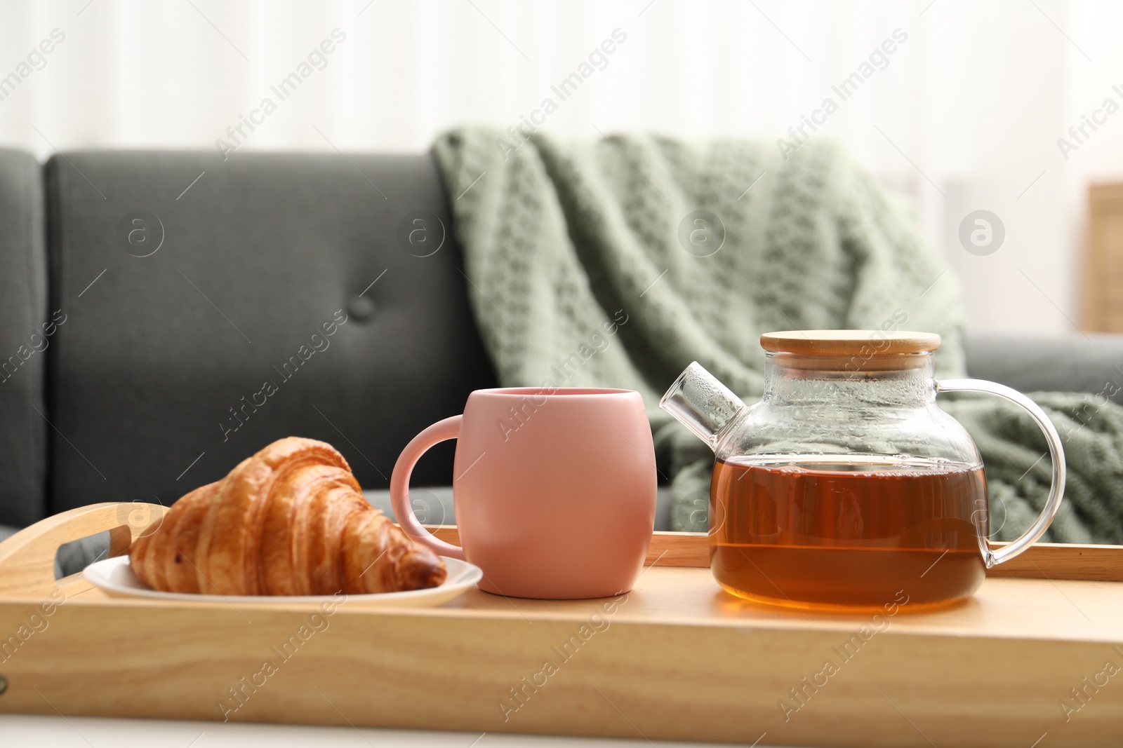 Photo of Aromatic tea in teapot, cup and tasty croissant on table indoors