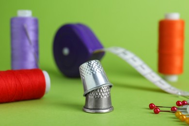 Thimbles and different sewing tools on green background, closeup