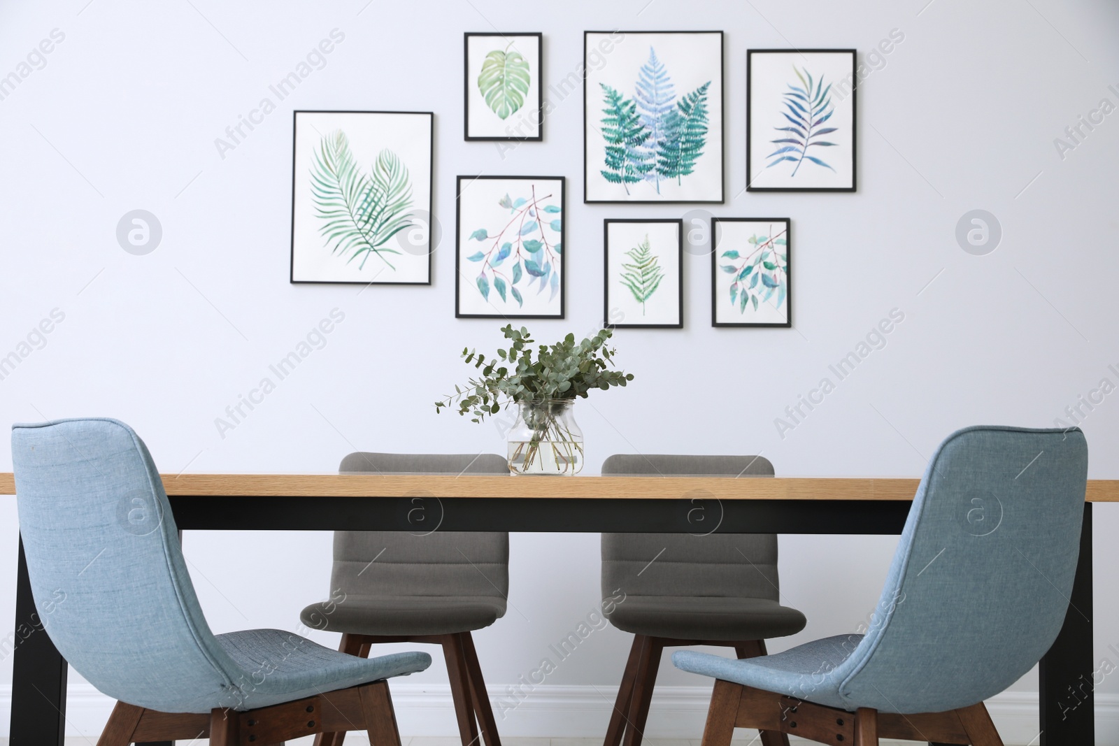 Photo of Stylish room interior with modern table, chairs and paintings of tropical leaves. Idea for design