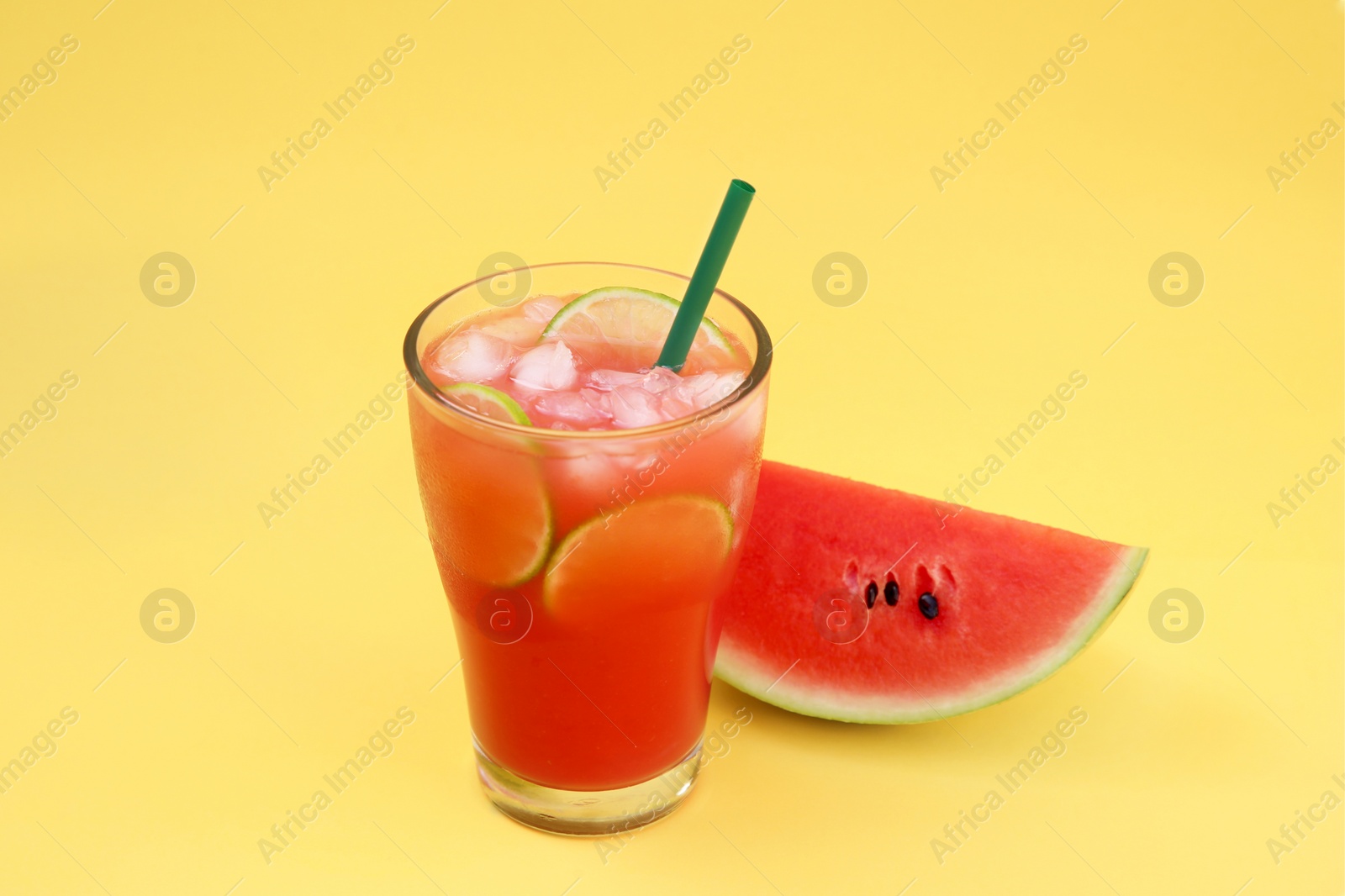 Photo of Glass of delicious drink with lime slices, ice cubes and fresh watermelon on yellow background