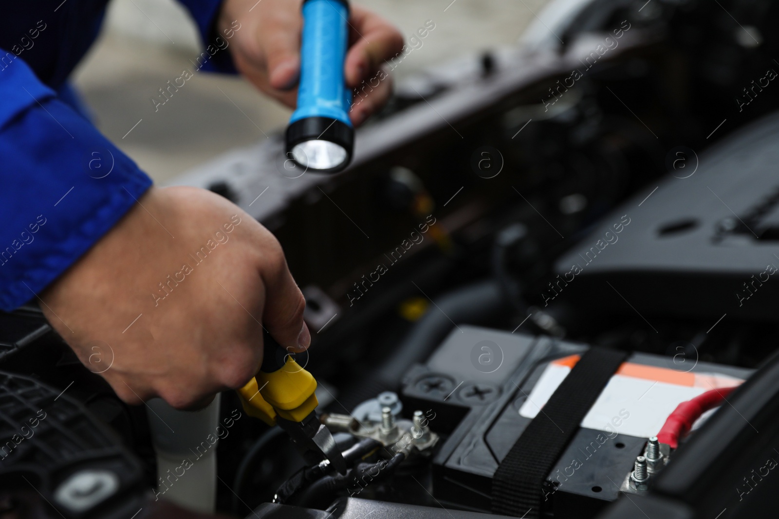 Photo of Mechanic with flashlight fixing car outdoors, closeup