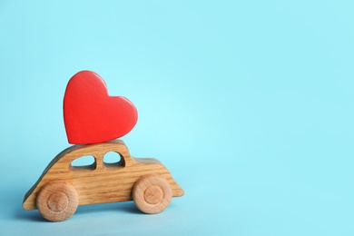 Small wooden car with heart on color background, space for text