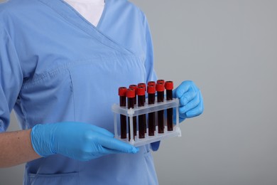Laboratory testing. Doctor with blood samples in tubes on light grey background, closeup. Space for text
