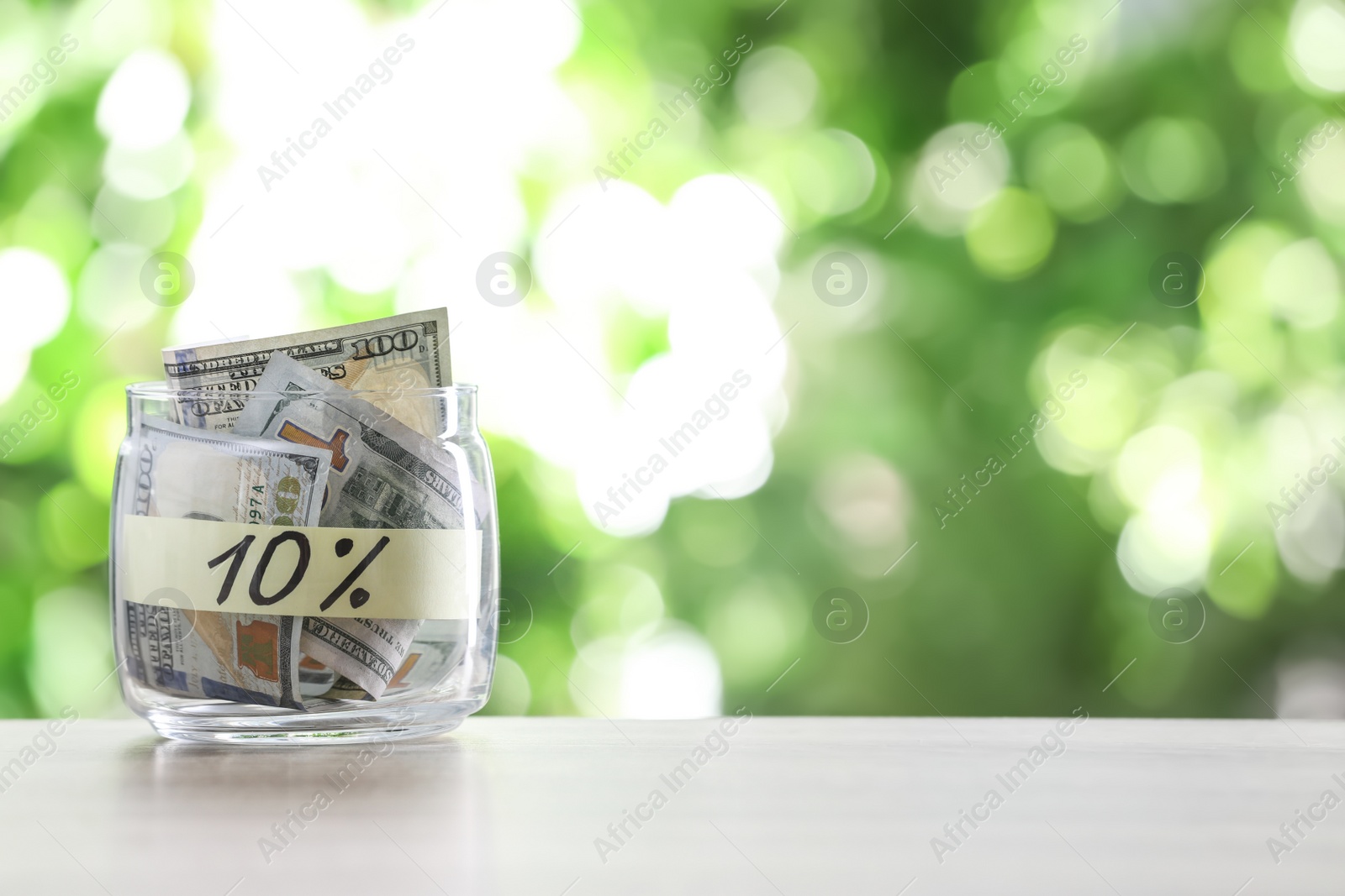 Photo of Glass jar with money and label 10 PERCENT on table against blurred background. Space for text