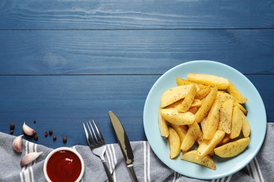 Photo of Plate of tasty baked potato wedges with spices and sauce on blue wooden table, flat lay. Space for text