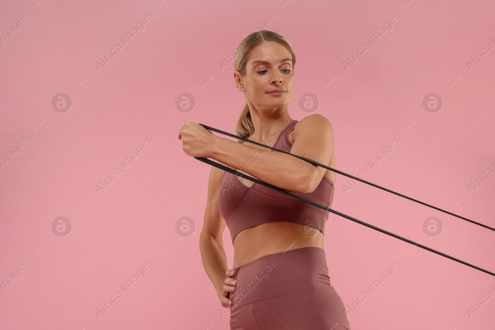 Photo of Woman exercising with elastic resistance band on pink background, low angle view. Space for text