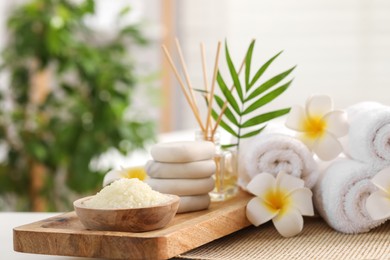 Photo of Composition with different spa products, plumeria flowers and palm leaves on table indoors, closeup