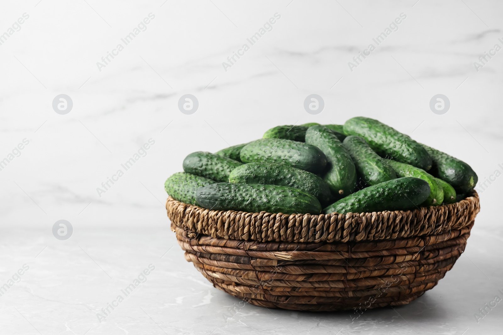 Photo of Fresh ripe cucumbers in wicker basket on marble table, space for text