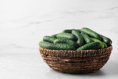 Photo of Fresh ripe cucumbers in wicker basket on marble table, space for text