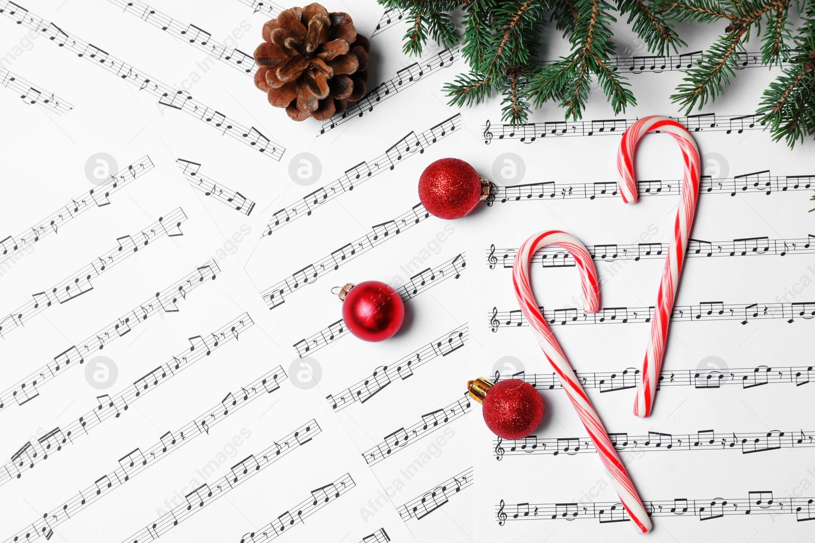 Photo of Composition with candy canes and Christmas balls on music sheets, top view