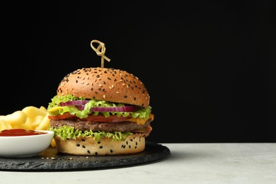 Photo of Burger with delicious patty, french fries and sauce on gray table against black background, space for text