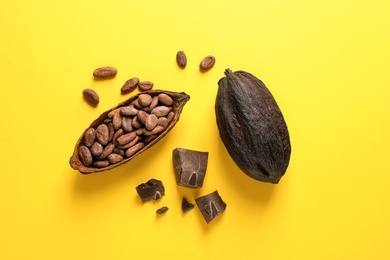Cocoa pods with beans and chocolate pieces on yellow background, flat lay