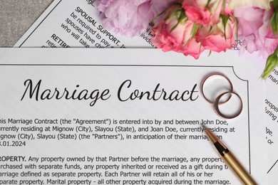 Photo of Marriage contract, wedding rings, pen and flowers on grey table, top view