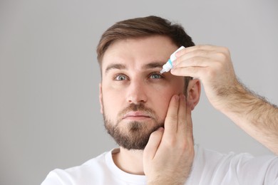 Photo of Young man using eye drops on light grey background