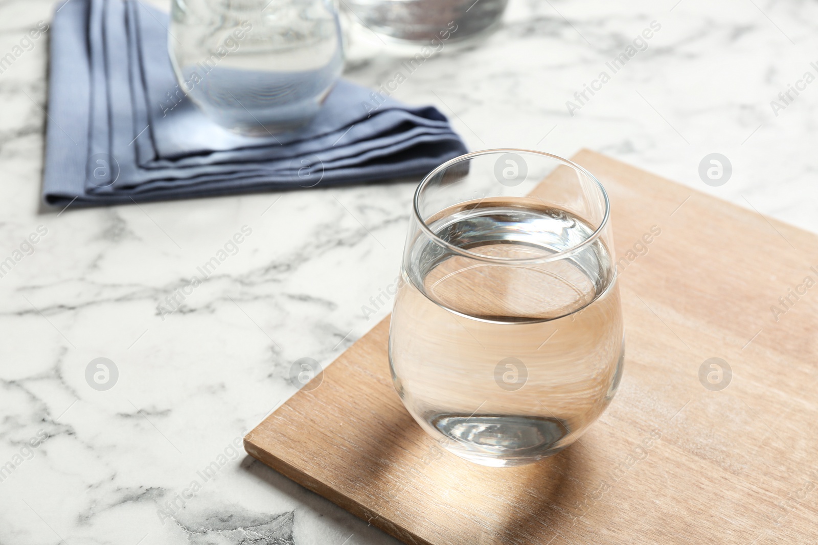 Photo of Wooden board with glass of fresh water on marble table. Space for text