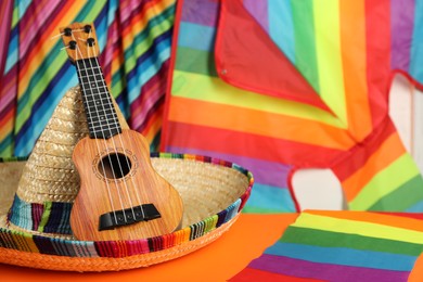 Photo of Mexican sombrero hat and ukulele on orange table, closeup. Space for text