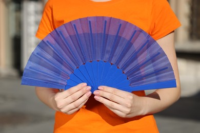Photo of Woman with blue hand fan outdoors, closeup