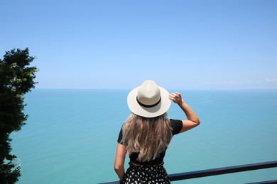 Photo of Woman with hat near sea on sunny day, back view