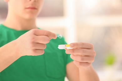 Photo of Teenage boy taking contact lens from container on blurred background