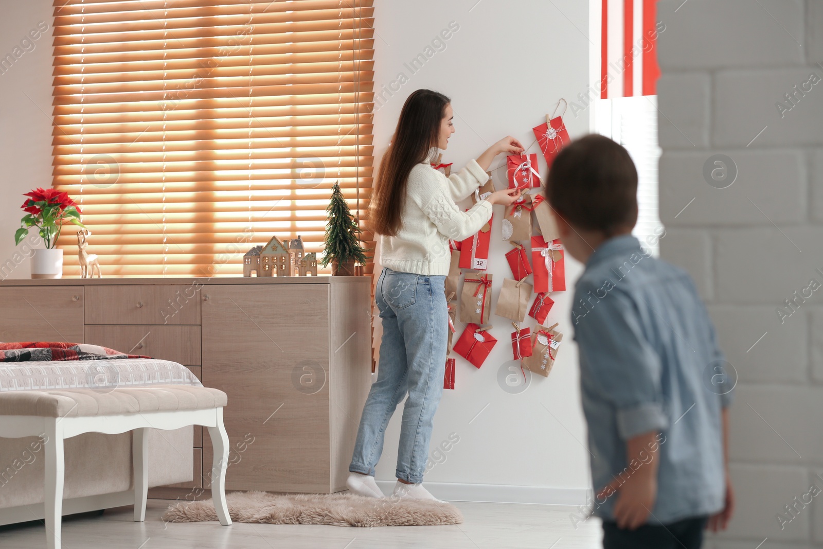 Photo of Little boy watching his mother taking gift from Advent calendar at home, back view. Christmas tradition