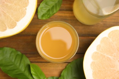 Glass of fresh pomelo juice, fruit  and green leaves on wooden table, flat lay