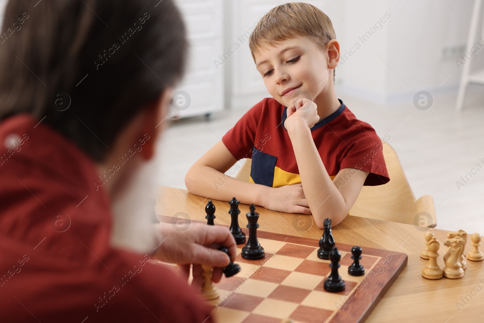 Photo of Little boy playing chess with his grandfather at table in room