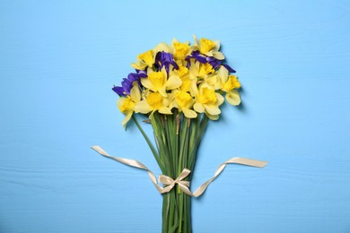 Photo of Bouquet of beautiful yellow daffodils and iris flowers on light blue wooden table, top view