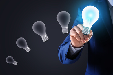 Image of Idea concept. Businessman touching glowing light bulb on virtual screen, closeup