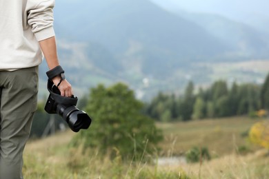 Photo of Photographer holding modern camera outdoors, closeup. Space for text