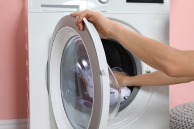 Photo of Woman putting laundry into washing machine indoors, closeup