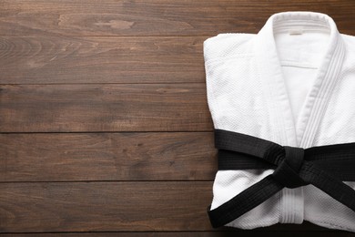 Photo of Martial arts uniform with black belt on white wooden background, top view. Space for text
