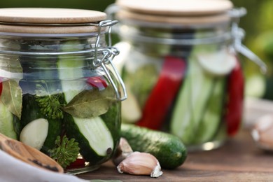 Photo of Jars of delicious pickled cucumbers on wooden table, closeup
