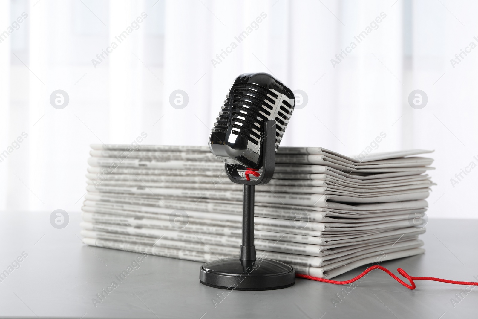 Photo of Newspapers and vintage microphone on grey table. Journalist's work
