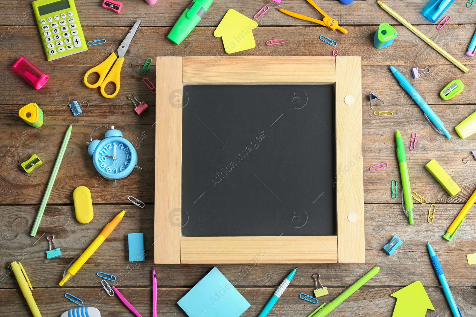 Photo of Different school stationery and blank small chalkboard on wooden background, flat lay. Space for text