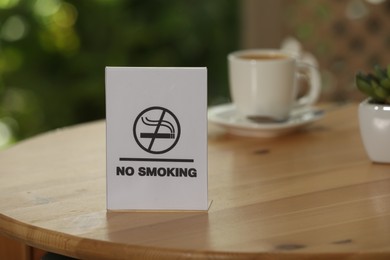 Photo of No Smoking sign on wooden table against blurred background