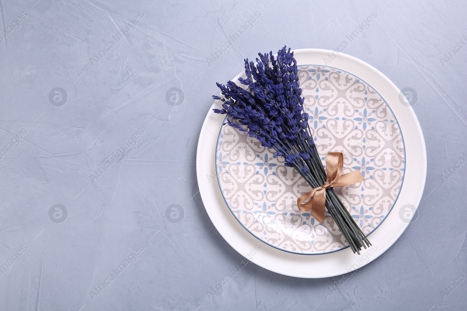 Photo of Bouquet of beautiful preserved lavender flowers and plates on light grey textured table, top view. Space for text