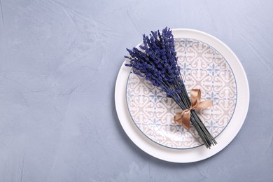 Photo of Bouquet of beautiful preserved lavender flowers and plates on light grey textured table, top view. Space for text