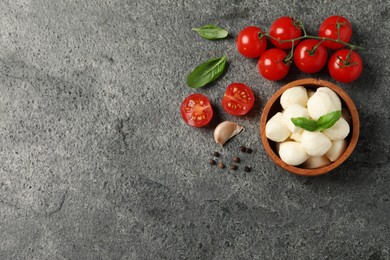 Photo of Delicious mozzarella balls in wooden bowl, tomatoes and basil leaves on light gray table, flat lay. Space for text