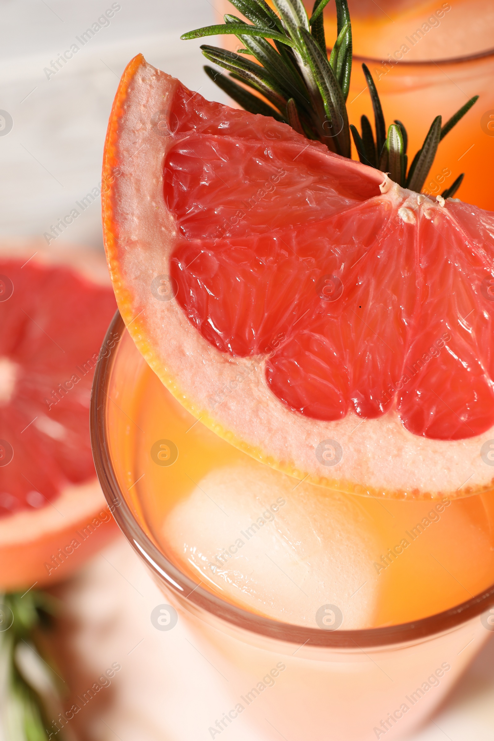 Photo of Tasty grapefruit drink with ice, rosemary and slice of fresh fruit in glass on table, closeup